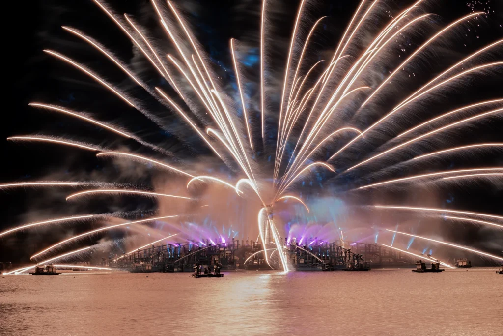 White fireworks spread in a wide symmetrical fan above the Epcot lagoon and show platform.