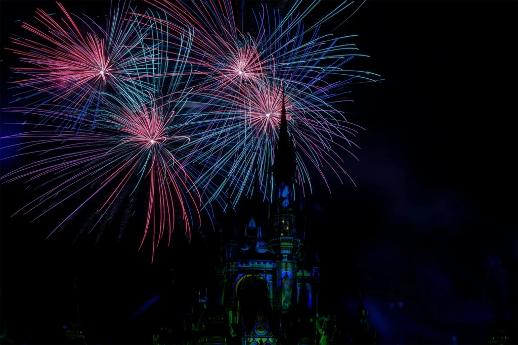 Pink, blue and turquoise fireworks burst above the castle during a nighttime Magic Kingdom show.